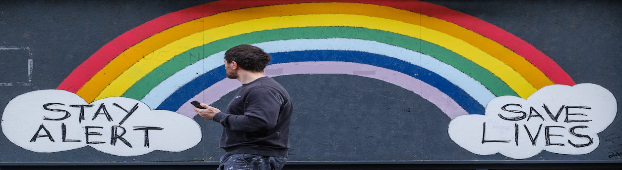 Graffiti on the wall reproduce a rainbow and the writing: "Stay alert, save lives". ILGA World uses this image to warn people against any potential fraud