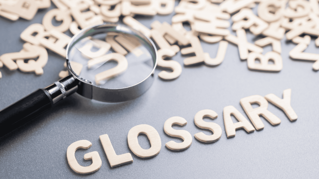 A group of wooden letters are scattered on a table, and a magnifying glass highlights some of them. Some other letters are grouped together to form the word "glossary"