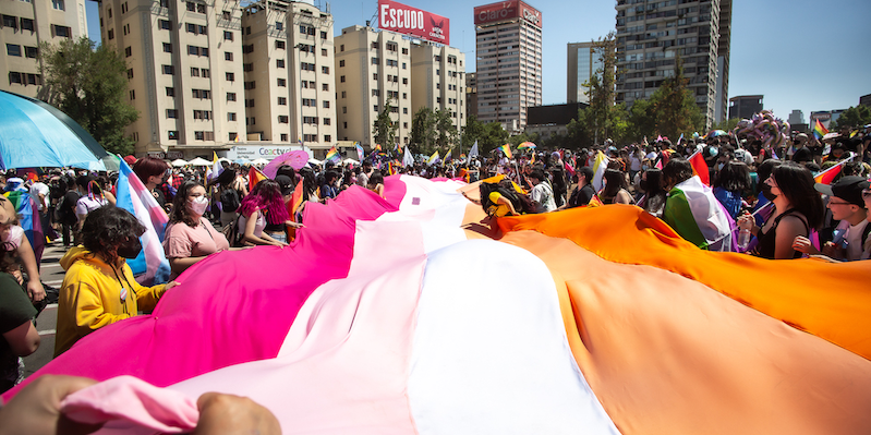 A crowd waves a lesbian Pride flag during a Pride march happening amidst high-rise buildings