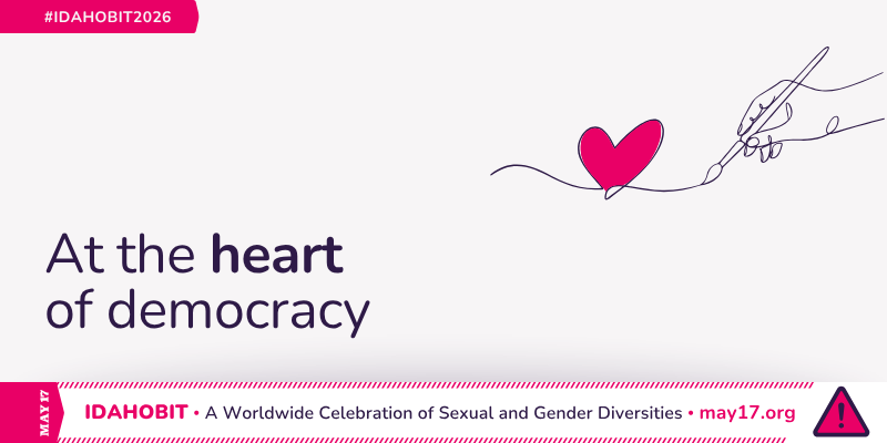 Line art of a hand holding a brush and drawing a heart. At the centre, the text reads "At the heart of democracy." A pink banner underneath includes "IDAHOBIT – A Worldwide Celebration of Sexual and Gender Diversities – may17.org" and the IDAHOBIT logomark, a pink triangle with an exclamation mark.