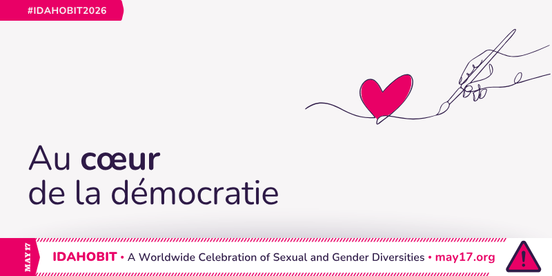 Dessin au trait représentant une main tenant un pinceau et dessinant un cœur. Au centre, on peut lire « Au cœur de la démocratie ». Une bannière rose en dessous indique « IDAHOBIT – Une célébration mondiale des diversités sexuelles et de genre – may17.org » et le logo IDAHOBIT, un triangle rose avec un point d'exclamation.