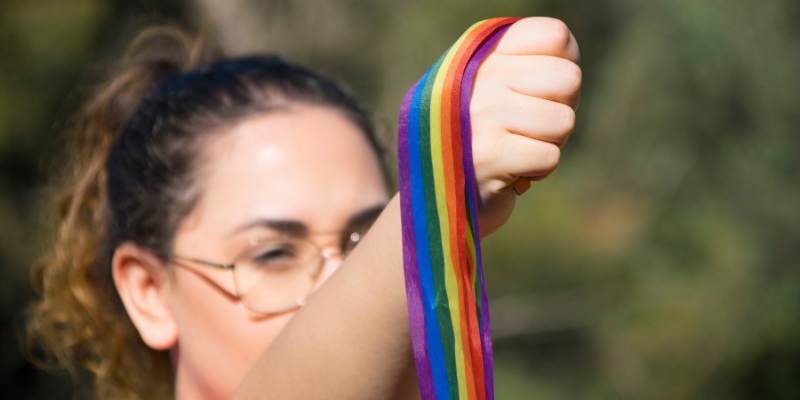 A queer woman holding stripes in the colours of a Pride flag