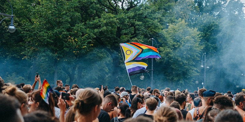 A group of people marching by the Tiergarten during Berlin Pride. An intersex-inclusive Progress Pride flag and a non-binary Pride flag are visible among the crowd