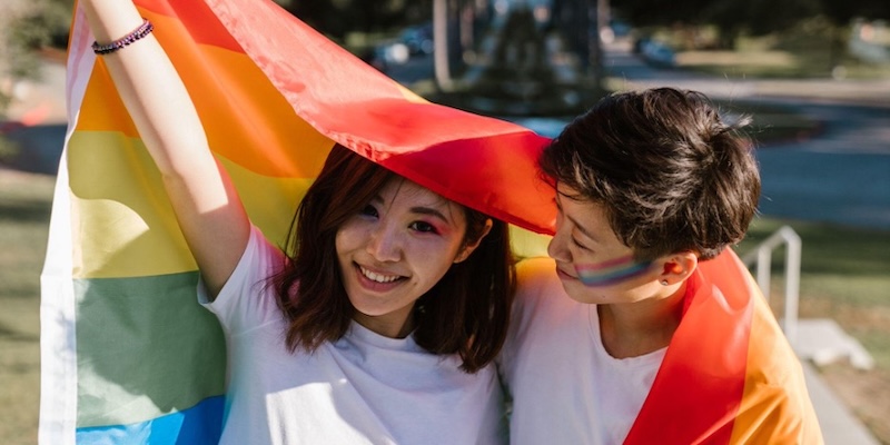 Two people embrace while holding a Pride flag