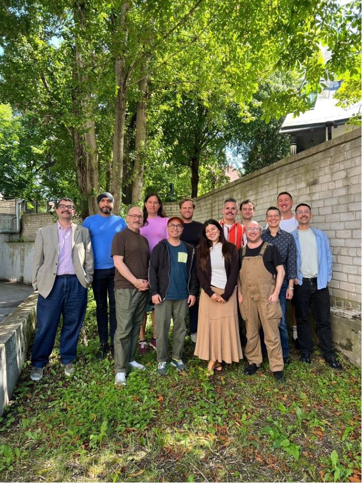 Group photo of participants from the LGBTI Pathways program gathered outdoors in Tallinn, standing together in front of trees and a brick wall.